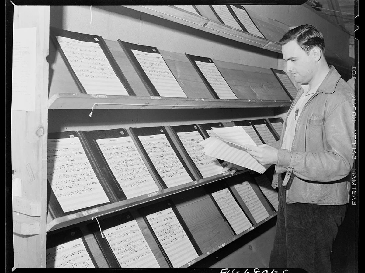 A National Music Camp staff member standing between tall racks of musical scores in the Interlochen music library in 1942.