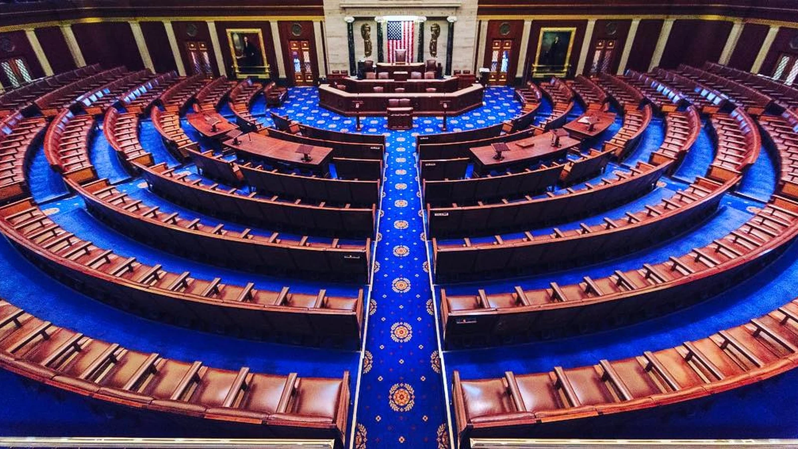 Empty U.S. House chamber viewed from the gallery, with the Speaker’s rostrum and voting boards visible.