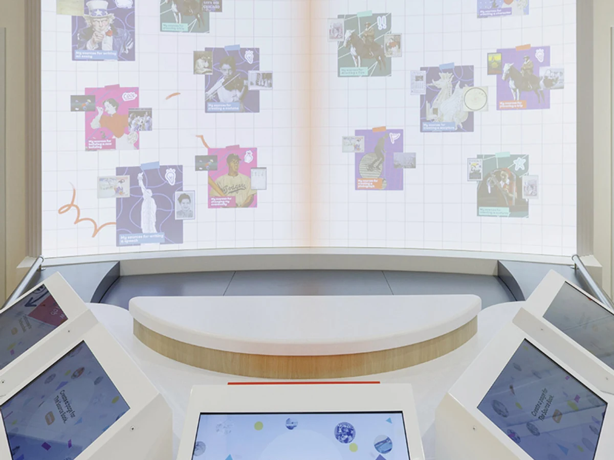 A large curved digital display shaped like an open book behind white touchscreen stations inside The Source.