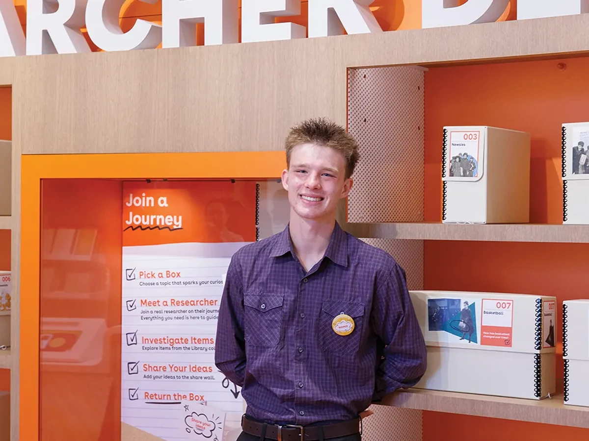 Weston Moats smiles in front of bright orange research shelves inside The Source gallery.