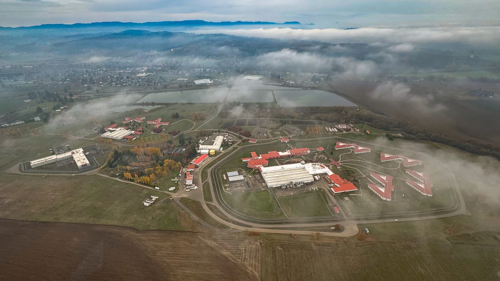 An aerial view shows a large federal correctional complex surrounded by fields and roads.