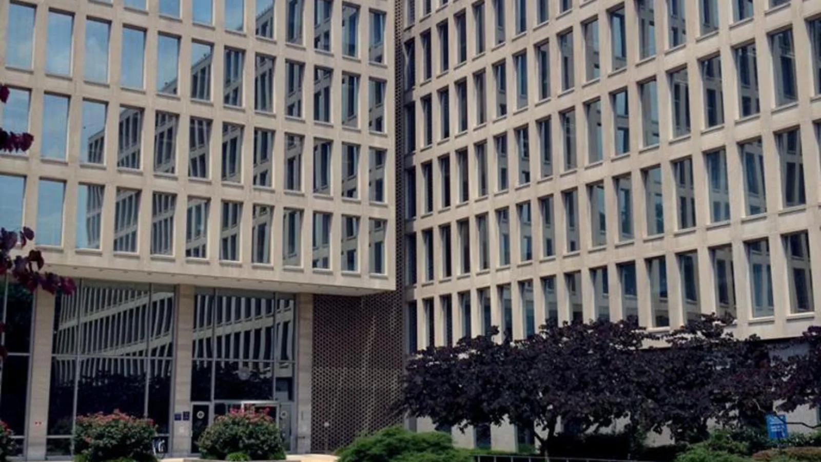 A broad concrete federal office building with a grid of windows stands behind landscaped grounds.