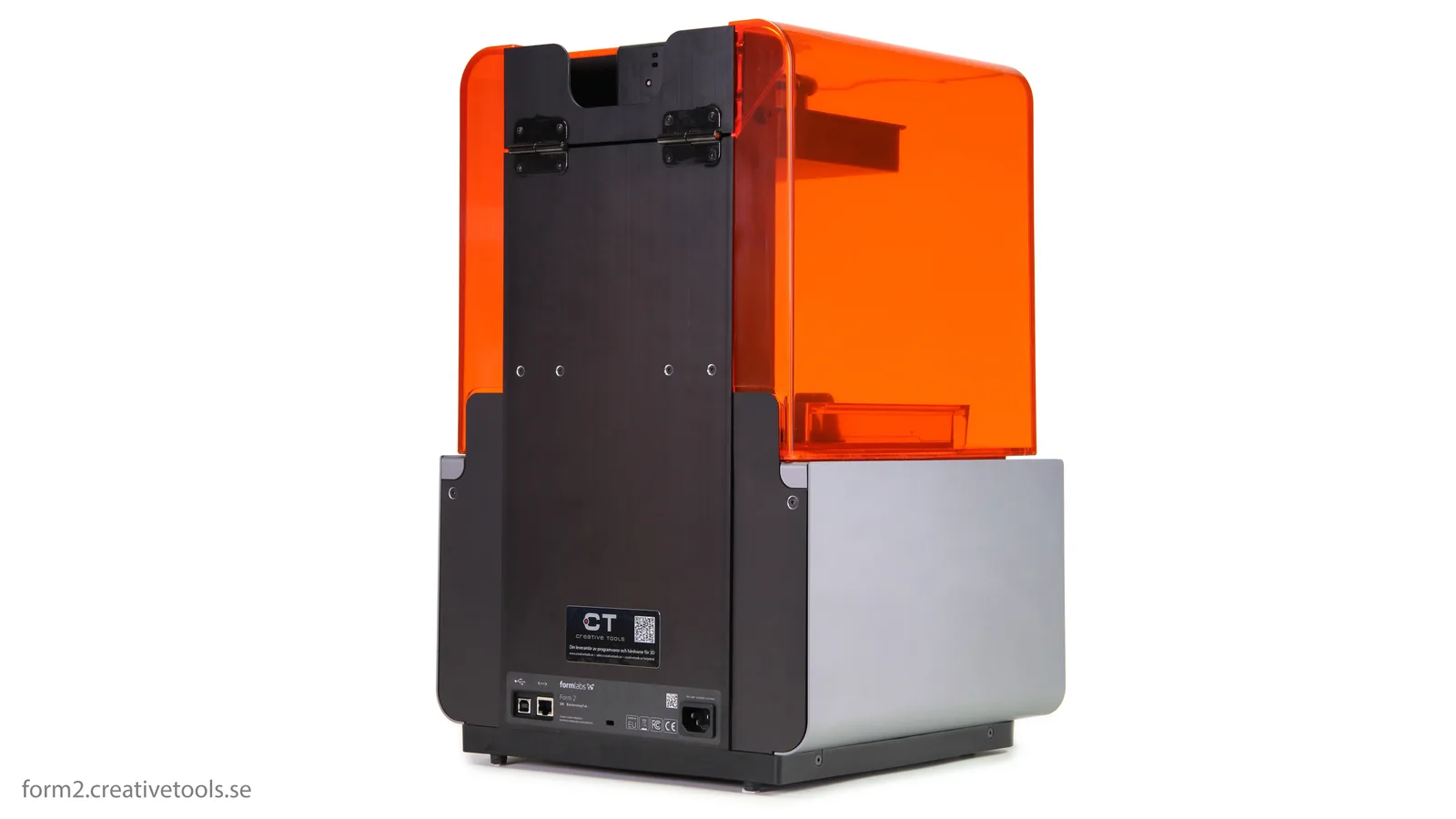 A desktop stereolithography 3D printer operates behind an orange-tinted cover in a workshop.