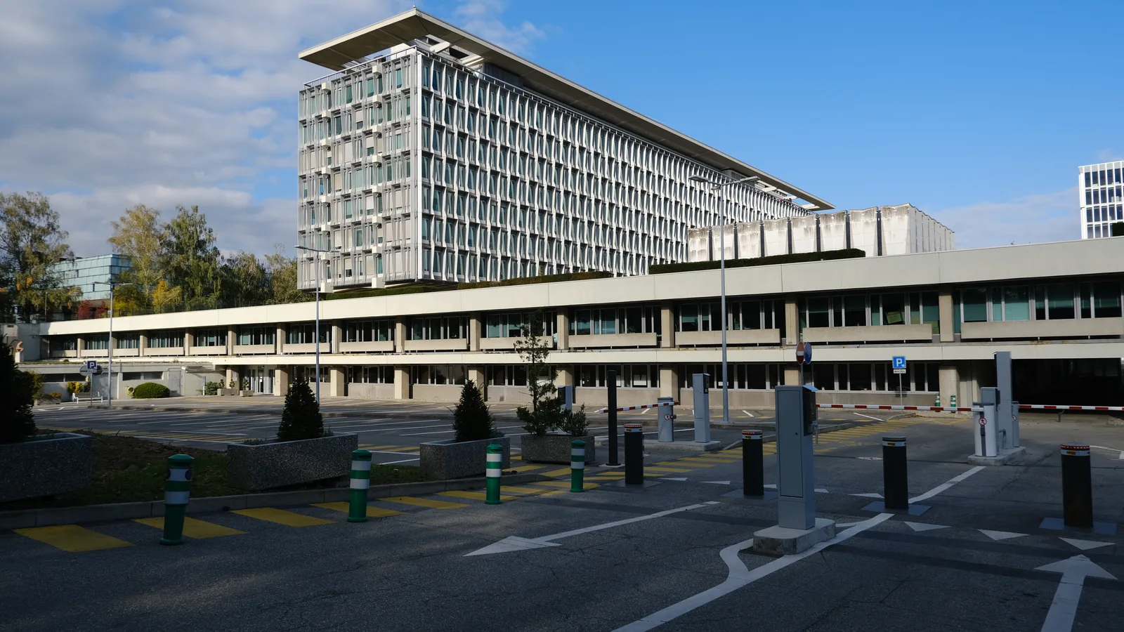 Modern World Health Organization buildings extend across a landscaped site beneath a blue sky in Geneva.