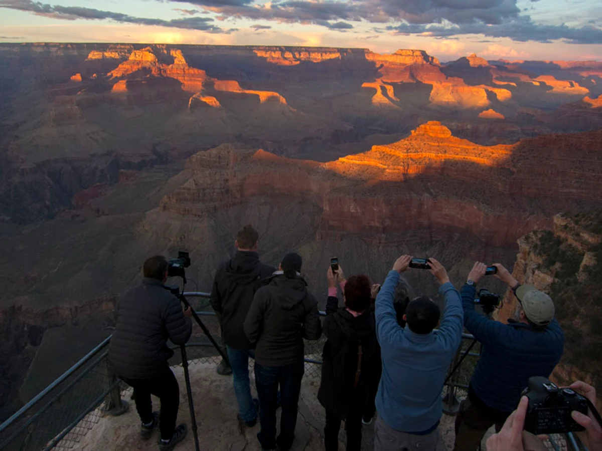 Visitors photograph a sunset-lit Grand Canyon from a rim overlook.